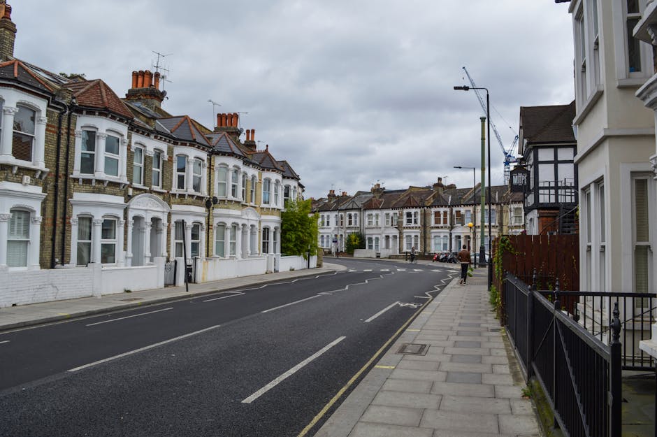 A quiet residential street in Tufnell Park with a row of terraced houses featuring white and brick facades, bay windows, and red tiled roofs on the left side, and a modern white building with black ac